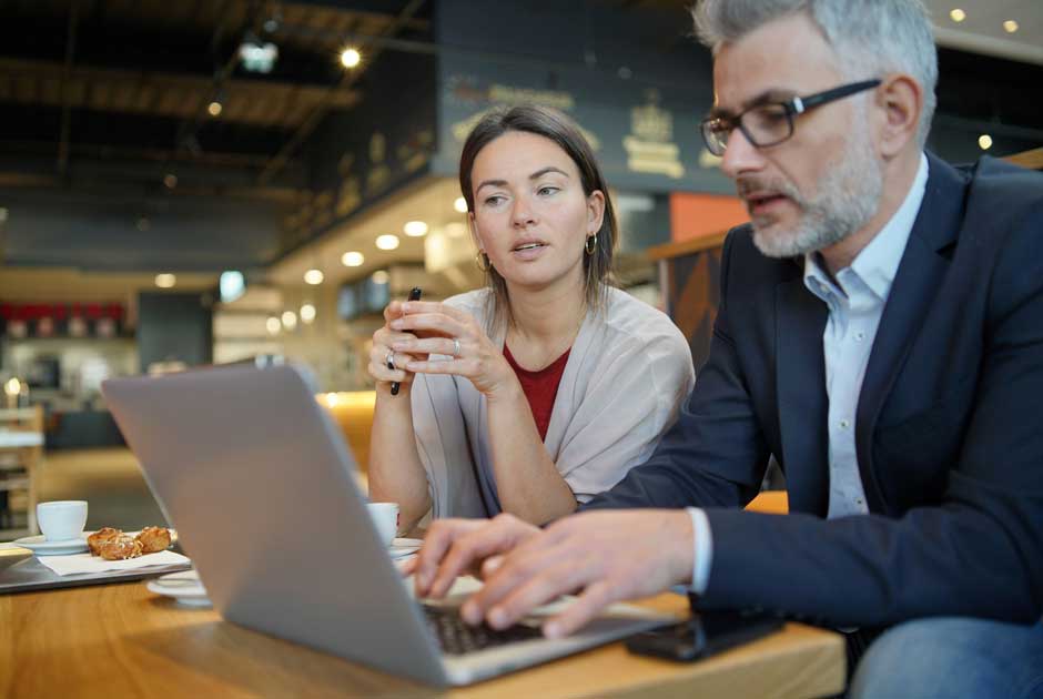 A pair of employees sit before a laptop, discussing survey results