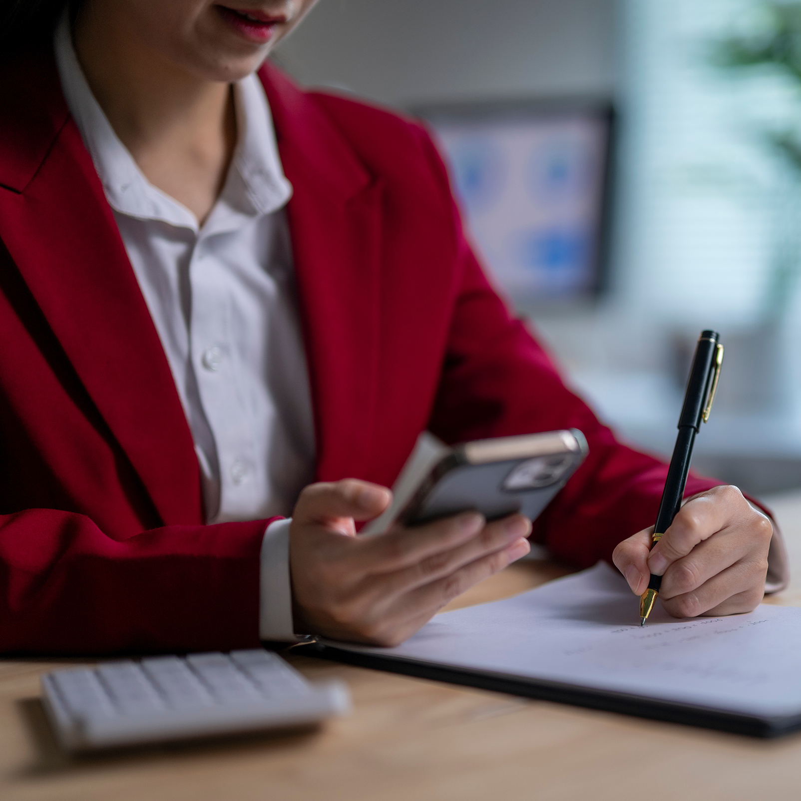 Woman in red blazer on the phone while taking notes
