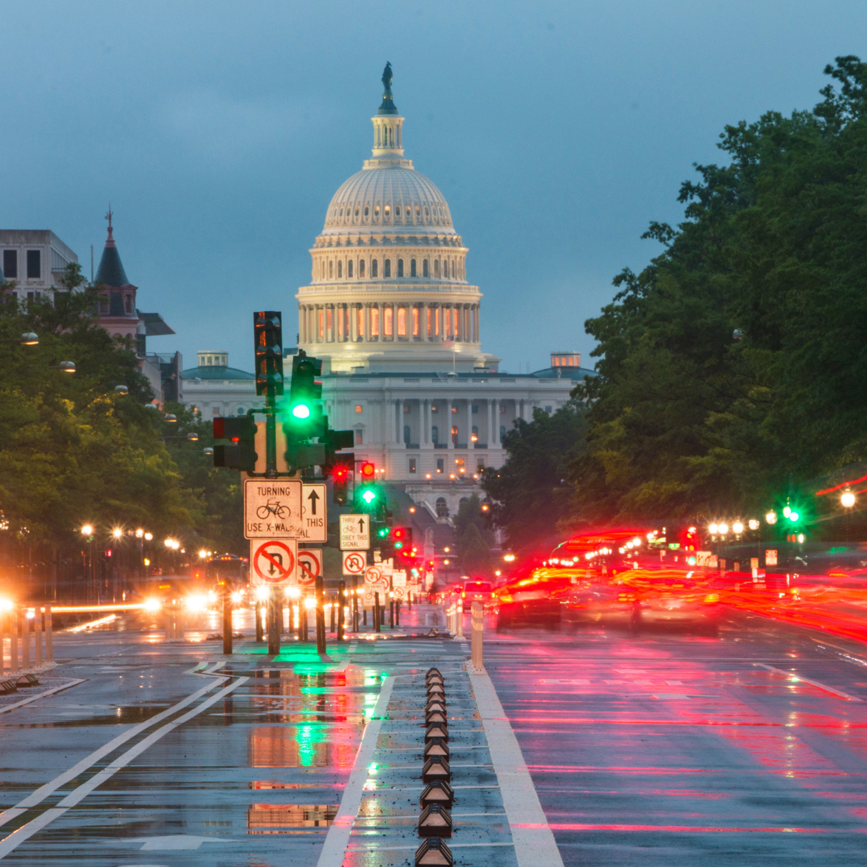 The U.S. Capitol building illuminated at night and seen via a busy, wet street
