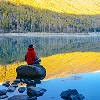 Woamn sitting and reflecting on rock near water