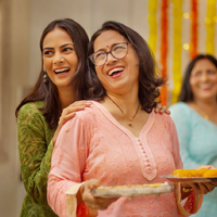 A grown Indian woman embraces her mother, who is carrying snacks at a party