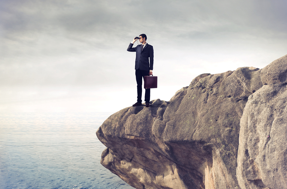 Businessman stands at the edge of a cliff and looks ahead