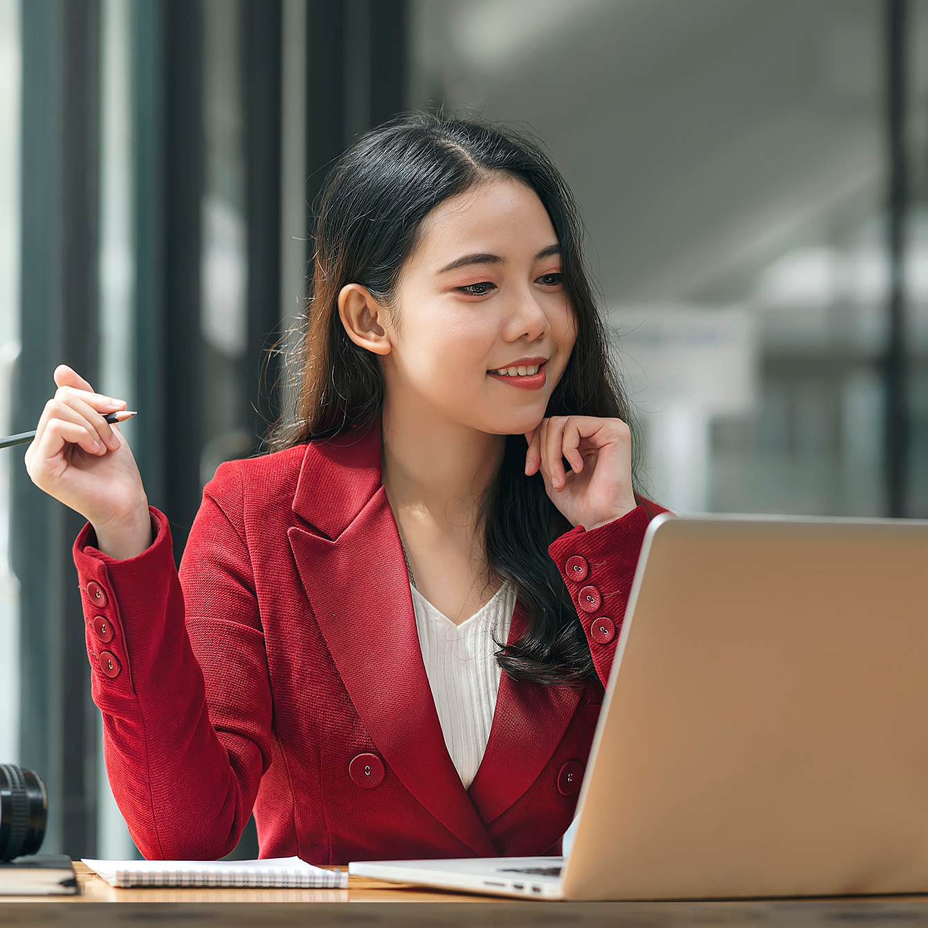 Woman looking at a computer screen with pen at the ready to take notes