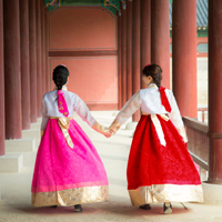 Two women in traditional Korean dresses walk hand-in-hand in a temple