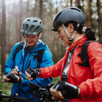 An older couple cycling in the woods pauses to check their fitness watches